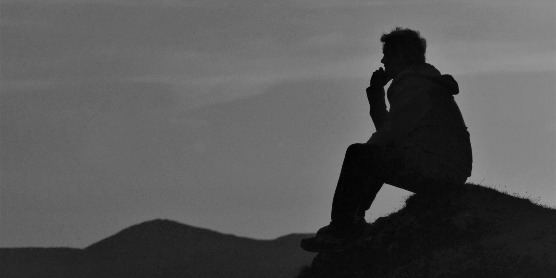 a man sitting on a hill and thinking